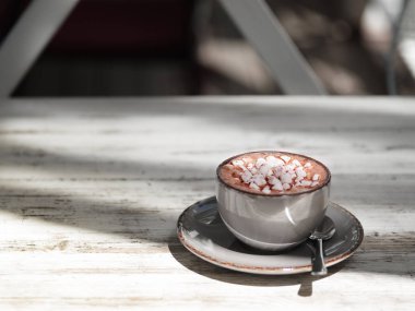 Lezzetli kapuçino gri ahşap masa arka plan üzerinde. Bir gri porselen kupa beyaz marshmallow ile tatlı kakao bardak tam bir yakın çekim resim. Metal bir kaşık ile bir fincan. Kopya alanı.