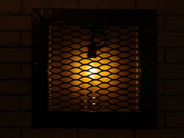 koyu kahverengi zemin ahşap bir çerçeve içinde metal parmaklıklar arkasında duvarında eski dekoratif lamba. 