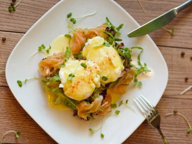 Çatal ve bıçakla bir ahşap masa arka planda bir plaka üzerinde şaşırtıcı haşlanmış yumurta bir görünüm yukarıdan. Tost ile yumurta, Balık eti, Yeşiller, mayonez ve baharat. İştah açıcı ev yapımı yemekler.