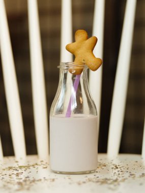 A stylish transparent bottle of a fresh lavender milk on a white table and on a blurred background. A sweet biscuit in the shape of a little man on a top of a jar. Healthy breakfast. clipart