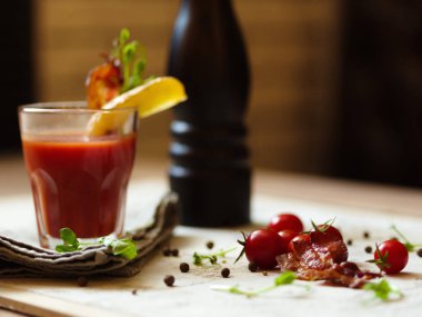 Bir yığın, cherry domates, baharatlı karabiber ve bir masada beyaz kumaş üzerinde yeşil otlar. Bir bardağın dolu kanlı Mary patates ve pastırma bir üst arka plan bulanık bir cam ile. Lezzetli aperatifler.