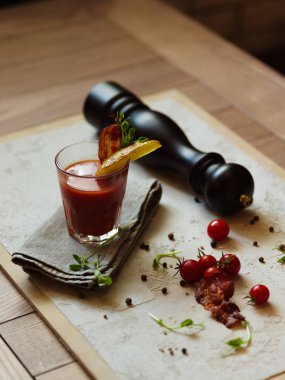 Organik domates, baharatlı karabiber, otlar ve karabiber değirmeni bir masada beyaz kumaş üzerinde. Bloody Mary bir bardak pastırma ve patates bir üst arka plan bulanık bir cam parçası ile.