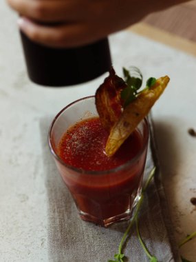 Bir alkol kokteyl sulu domates biber ve votka bir bez ve beyaz arka plan üzerinde bir biber değirmen tutan bir kadın eli sprinkles. Bloody Mary kokteyl ve aperatifler tepesinde bir cam.