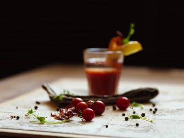 Bir yığın doğal kiraz domates, baharatlı peppercorns ve yeşil otlar hafif bir kumaş ve bir siyah arka plan bulanık. Bloody Mary pastırma ve patates tepesinde bir cam parçası ile bir bardak.