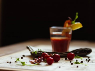 Bir yığın doğal kiraz domates, baharatlı peppercorns ve yeşil otlar hafif bir kumaş ve bir siyah arka plan bulanık. Bloody Mary pastırma ve patates tepesinde bir cam parçası ile bir bardak.
