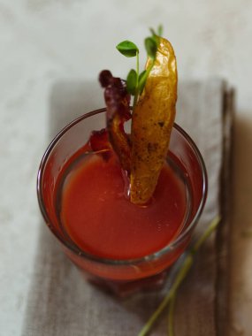 Bir üst kiraz domates votka ile taze meyve suyu görünümünün bir hafif kumaş ve arka plan bulanık. Patates, lezzetli domuz pastırması ve baharatlı bitki bir cam alkol içecek ile tepesinde bir parça.