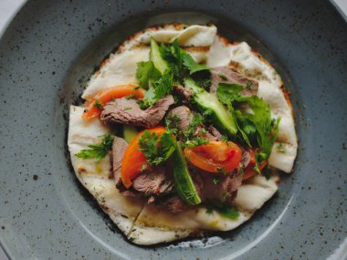 Bir mavi yuvarlak tabak dolusu parlak yemeğin bir arka plan olarak bir görünüm yukarıdan. Sığır eti, salatalık, domates, maydanoz ve pide ekmek ile lezzetli bir meze. Lezzetli pahalı yiyecek. Restaurant konseptini.