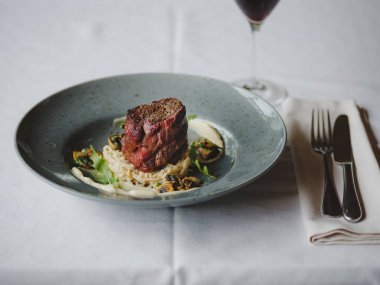 Bir mavi yuvarlak tabak lezzetli yemeğin yanında yemek servisi ve bir şarap kadehi bulanık Restoran arka plan üzerinde tam bir yakın çekim resim. Lezzetli pahalı yiyecek. Restoran, yiyecek konsepti.