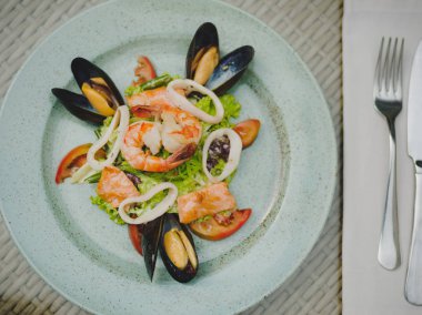 Taze karides, midye, domates, salata yaprağı. Güzel tabak büyük bir ışık plaka üzerinde. Profesyonel, mevsimlik mutfak. Egzotik yemek pahalı bir restoranda. Masanın üzerinde bir çatal ile bir tabak.