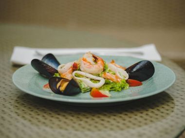 Taze karides, midye, domates, salata yaprağı. Güzel tabak büyük bir ışık plaka üzerinde. Profesyonel, mevsimlik mutfak. Egzotik yemek pahalı bir restoranda. Masaya bir tabak.