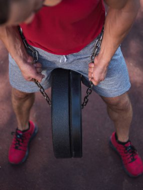 Seksi vücut ile güçlü bir adam kendi ayakları üzerinde egzersizleri yapıyor. Yakışıklı bir genç adam parkta ayaklarıyla ağırlık kaldırıyor.