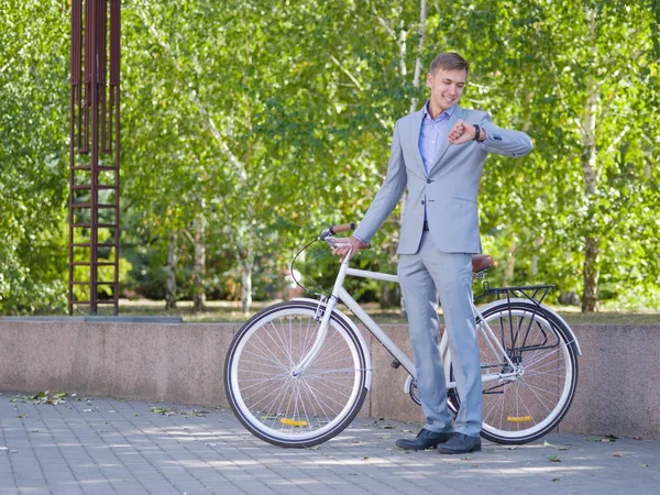 Un tipo con su bicicleta blanca está caminando por la calle contra el telón de fondo de árboles verdes — Foto de Stock