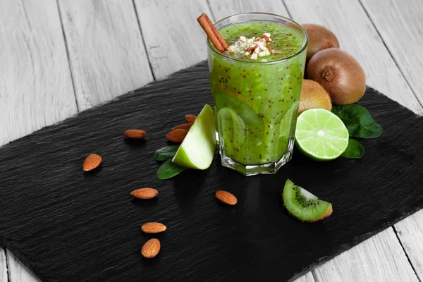 Kalın, kivi milkshake sulu limes ile harmanlanmış ve siyah bir tepsi üzerinde elma kesti. Baharatlar ve ahşap masa arka plan üzerinde fındık ile taze bir alkolsüz içecek. Doğal kompozisyon.