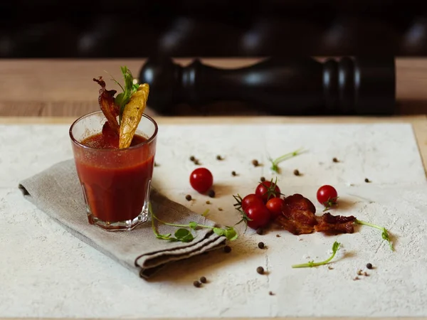Küçük domates, karabiber, otlar ve karabiber değirmeni üst görünümünü ahşap bir masa üzerinde hafif kumaş üzerinde. Bloody Mary bir bardak pastırma ve patates bir üst arka plan bulanık bir cam dilim ile.