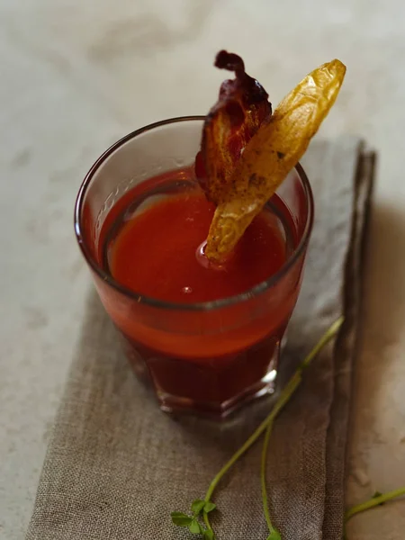 Bir üst kiraz domates votka ile taze meyve suyu görünümünün bir hafif kumaş ve arka plan bulanık. Patates, lezzetli domuz pastırması ve baharatlı bitki bir cam alkol içecek ile tepesinde bir parça.