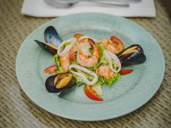 Taze karides, midye, domates, salata yaprağı. Güzel tabak büyük bir ışık plaka üzerinde. Profesyonel, mevsimlik mutfak. Egzotik yemek pahalı bir restoranda. Masaya bir tabak.