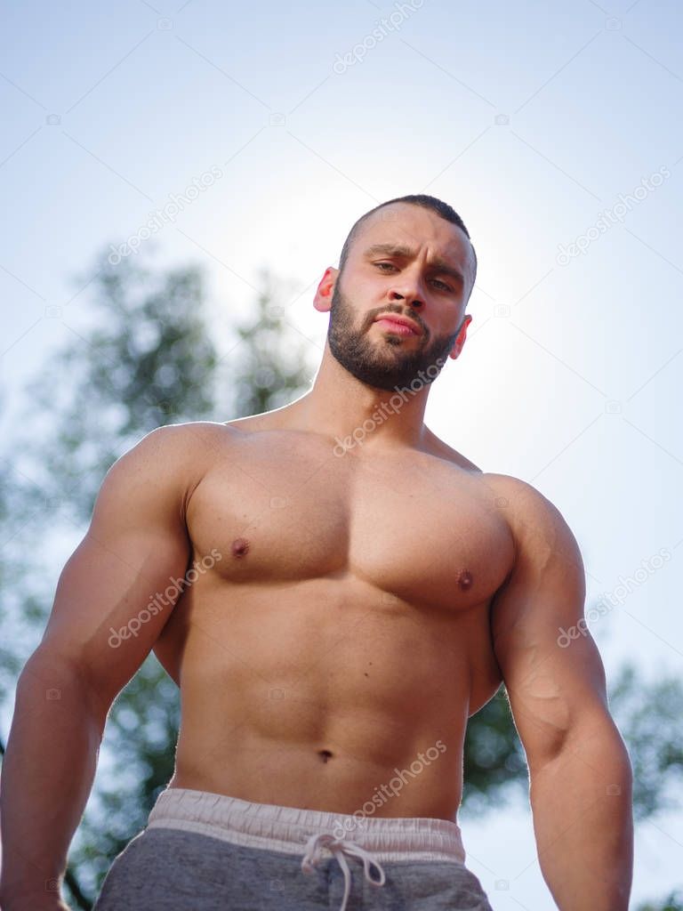 Sexy and muscular shirtless bodybuilder man showing off on a blurred background. Working out concept.