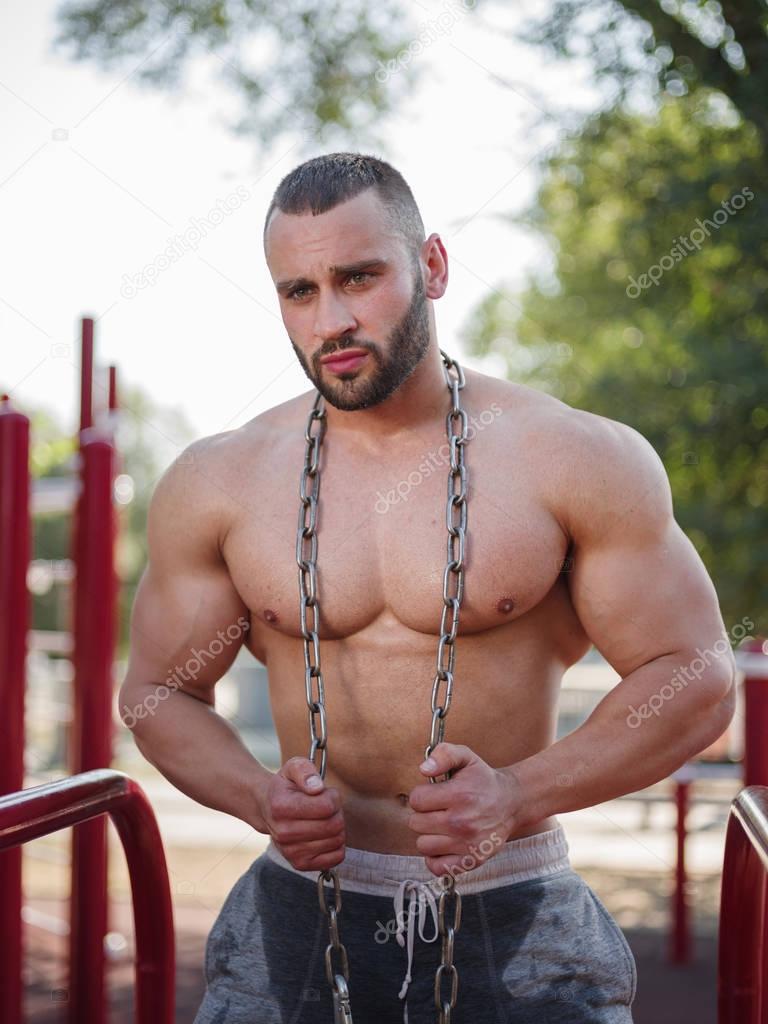 Handsome, healthy, muscular sports man with a metal chain on a blurred background. Heavyweight concept.