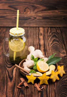Yeşil çay limon dilimi ve sarı saman ahşap zemin ile bir mason kavanoz bileşimi. Kahverengi bir plaka ile kesilmiş limon, zencefil, nane, tarçın ve bir masa üzerine carambola yıldız.