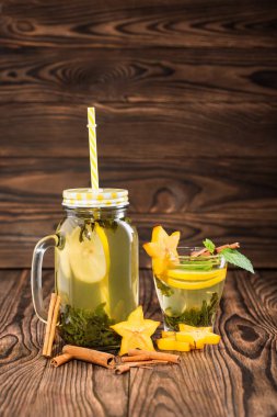 Mason jar sarı saman ile limon çay ve yeşil çay nane ve hafif ahşap arka plan üzerinde tropikal carambola bileşimi. Tarçın ve meyve sağlıklı ev yapımı çay. Kopya alanı.