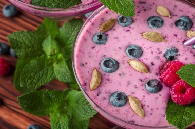 İki margarita gözlük smoothies ahşap arka plan üzerinde yenileme tam üst bir bakış. Sağlıklı kokteyller yoğurt, ahududu, yaban mersini ve nane yaprakları ile karışık. Vegan içecekler.