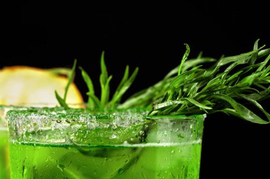 Lezzetli ve serinletici alkol içecek parlak baharatlı tarhun ve buz küpleri ile close-up. Siyah bir zemin üzerine uzun bir bardak meyveli kokteyl. Soğuk içecek ve kesme sulu kavun.