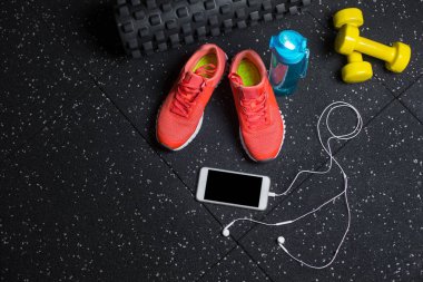 Benekli bir siyah arka plan üzerine yukarıdan görünüm renkli Eğitim ayakkabı, parlak sarı dambıl, spor şişe su ve kulaklık ile smartphone. Rahat kadın spor malzemeleri.