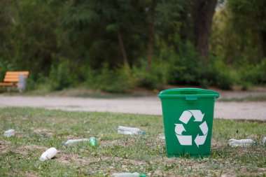 Bir plastik çöp kutusu yanında doğal arka plan bulanık plastik şişe geri dönüşüm işareti. Bir parlak yeşil geri dönüşüm kutusu parkta. Ekoloji, çevre, kirliliği kavramı.