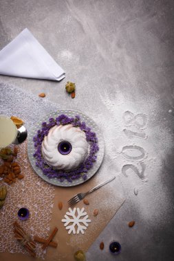 Üstten Görünüm Noel kek mor çiçekler, baharat ve pudra şekeri ve fantezi süslemeleri ile güzel bir kompozisyon. Festival çanak ve yazılı 2018 bir masa lambası arka plan üzerinde oturum açın. Kopya alanı.