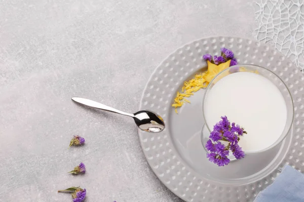 A view from above on a plate with a healthful non-alcoholic smoothie, purple flowers and a spoon on a white background. Vegetarian homemade desserts with milk and fruits. Copy space.