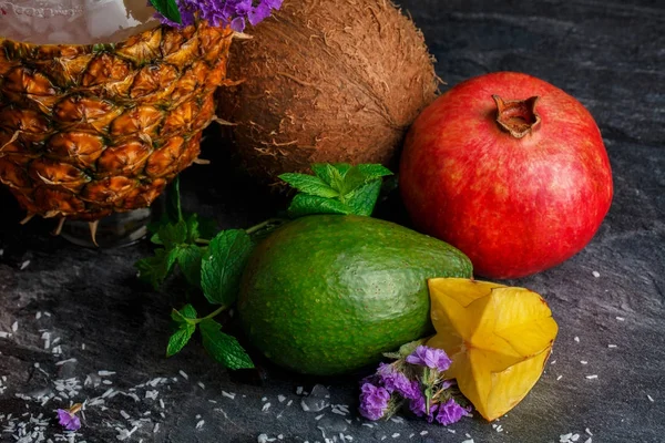 Bir tropikal bir ananas yukarıdan görünüm, olgun garnet, yeşil avokado ve egzotik Hindistan cevizi koyu gri arka plan üzerinde. Organik meyve besleyici vitaminler tam bir bileşimi.