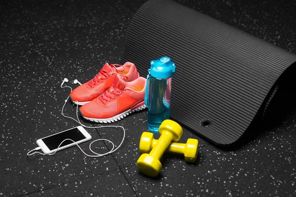 Küçük sarı dambıl, pilates mat, mavi şişe su, parlak pembe eğitmenler ve modern beyaz smartphone handphones siyah bir arka plan ile dolu. Spor ve eğitim kavramı. Kopya alanı.