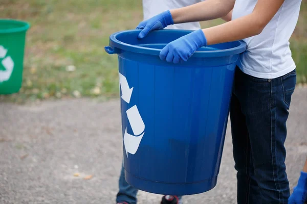 一张儿童手捧着一个深蓝色回收容器的特写照片 儿童收集塑料垃圾在一个模糊的自然背景 自然污染的概念 复制空间 — 图库照片