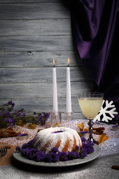 Güzel bir sofra üzerinde gri bir ahşap arka plan tatil gıdalardan. Geleneksel ev yapımı kek tatlı krema ve bir plaka üzerinde dekoratif çiçek. Ananas suyu ve bir masada uzun mumlar.