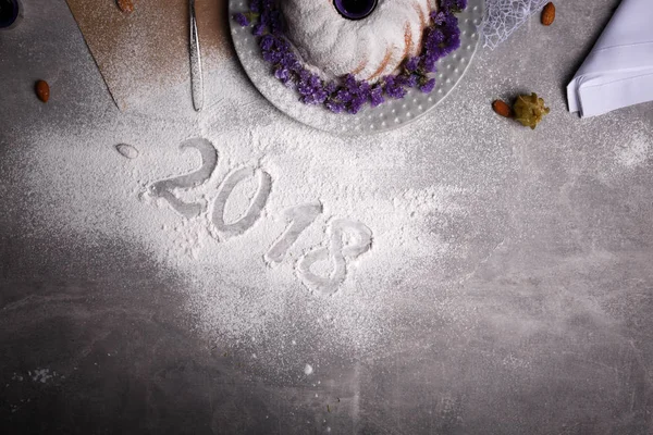 Gelen dondurulmuş tablo arka plan üzerinde şenlikli bir geleneksel Noel kek yanındaki 2018 işareti yukarıda görüntüleyin. Doğal, güzel, ev yapımı kek egzotik baharatlar ve çiçekler ile dekore edilmiştir. Kopya alanı.