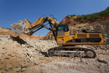 Yakın çekim büyük Ekskavatör bir mavi gökyüzü ve kumlu taş ocağı arka plan yere yükleme. 