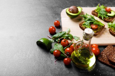 Bir şişe zeytinyağı ve sağlıklı bir kahvaltı için sebze dolu close-up. Ekmek, avokado, kesilmiş domates, roka kahvaltı sandviç parlak tablo arka plan üzerinde yanındaki yeşil. Kopya alanı.