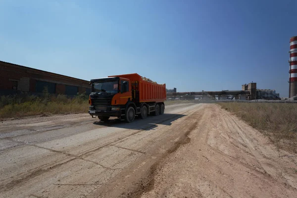 Makine ekipman ile bir doğal kum ocağı arka plan yüklü bir yere. Sürüş kumlu bir yolda bir büyük portakal ışınlama. Teknoloji, kargo, ticaret, ulaşım kavramı. Kopya alanı.