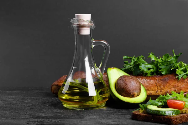 A colorful set of natural ingredients: a jar of olive oil, juicy avocado, salad leaves and a crusty bread on a stone table background. Healthy, appetizing avocado toast for a school lunch. Copy space.