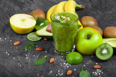 Rendelenmiş badem ve koyu gri taş zemin üzerine tropikal meyve ile taze kivi güler yüzlü bir organik bileşimi. Sarı bir dalı muz, elma, avokado ve kivi bir masada kesmek.