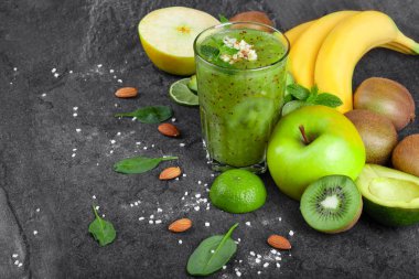 Rendelenmiş badem ve koyu gri taş zemin üzerine tropikal meyve ile taze kivi güler yüzlü bir organik bileşimi. Sarı bir dalı muz, elma, avokado ve kivi bir masada kesmek.