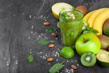 Renkli bir kompozisyon bir organik kivi güler yüzlü bir kara günü rendelenmiş badem ve tropikal meyve ile arka plan taşlar. Bütün ve kesilmiş elma, kivi, avokado ve bir tablo üzerinde sarı muz dalı.