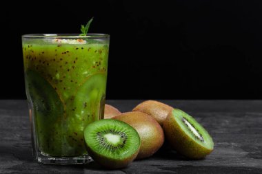 Kivi ve nane ile güler yüzlü bir kompozisyon bir gri taş tablo ve doymuş bir siyah arka plan üzerine bırakır. Bir yığın organik kivi meyve yakınındaki bir masa üzerine yeşil bir içecek. Besleyici Kahvaltı.