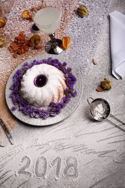 Yukarıdan bir Noel pudingi ile pudra şekeri serpilir ve açık gri renkli çiçekler ile dekore edilmiştir. Bir tatil 's kek, Hindistan cevizi sütü ve bir tablo üzerinde bir elek. Yılbaşı Dekorasyonu. 