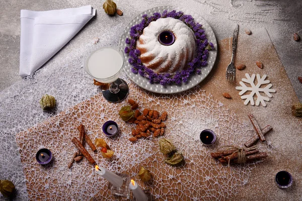 Güzel bir yeni yıl kompozisyon kahverengi ve gri kumaş arka plan üzerinde. Buzlanma ile geleneksel ev yapımı kek ve dekoratif çiçek tabakta, üstten görünüm. Bir içki, tarçın, badem, bir masa üzerine mumlar.