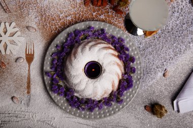 Kahverengi ve gri kumaş arka plan üzerinde güzel bir yeni yıl kompozisyon bir görünümünü yukarıda. Buzlanma ile geleneksel ev yapımı kek ve bir plaka üzerinde dekoratif çiçek. Kış içki ve bir masa üzerine badem.