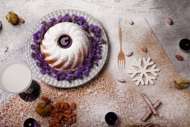 Yukarıdan bir kompozisyon bir geleneksel Noel Pasta krema ve mor çiçekler etrafında bir plaka ve renkli arka plan üzerinde pişmiş yemek. Bir Hindistan cevizi içecek ve bir yığın bir masa üzerine badem.