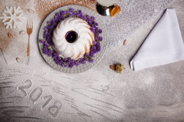 Vanilyalı pasta Menekşe çiçek ve mum bir merkezindeki Noel tatili için en iyi görünümü gri bir arka plan üzerinde. Bir soğuk içecek, peçete ve kar tanesi üzerinde gri bir tablo. Kopya alanı.