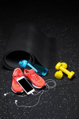 Mavi bir şişe su, mat, parlak pembe Eğitim ayakkabı, fiziksel egzersizler ve modern telefon handphones ile sarı araçlar germe benekli bir siyah arka plan üzerine siyah yakın çekim resim.