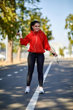 Genç gülümseyen kadın parkta ip atlıyor.